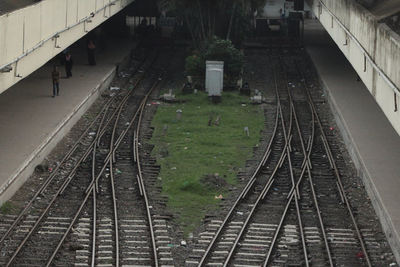 Converging train tracks in an urban station with platforms and people.